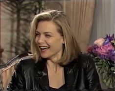 a woman sitting in a chair laughing and looking at the camera while wearing a black leather jacket