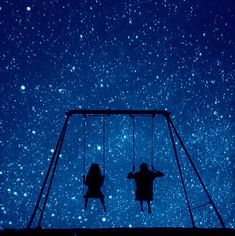 two people sitting on swings in the sky at night with stars above them and one person standing