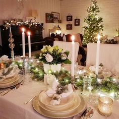 a dining room table set for christmas dinner with candles and greenery on the table