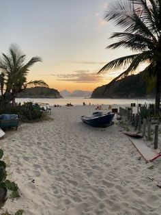 a beach with boats and palm trees on it at sunset or sunrise in the distance