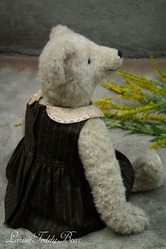 a white teddy bear wearing a black dress sitting on the ground next to yellow flowers