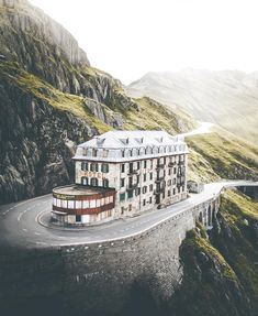 an old building sitting on the side of a mountain road with a curved street below it