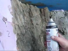 a person is holding a spray paint in front of a rock wall that has been painted