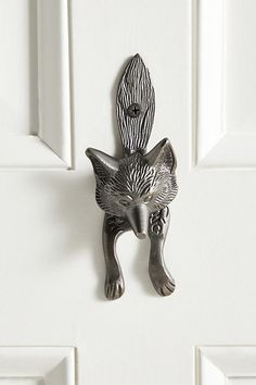 a door handle with a cat design on it's front and back sides, hanging from the side of a white door