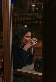 a woman sitting at a table with her hand on her mouth and looking out the window