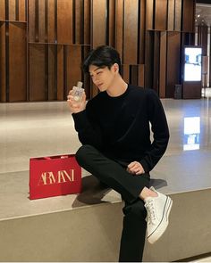 a young man sitting on top of a stone bench holding a bottle of perfume in his hand