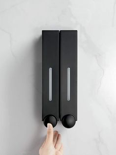 a hand is pressing the button on a black wall mounted toilet paper dispenser