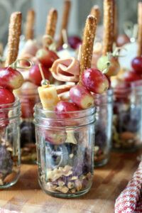 several jars filled with food on top of a wooden table covered in nuts and pretzels