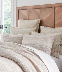 a bed with white linens and pillows in a bedroom next to a wooden headboard