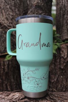 a blue coffee cup sitting on top of a tree trunk with the word grandma written on it