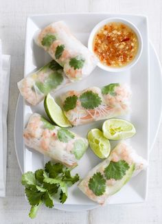 shrimp rolls with dipping sauce and cilantro on a white plate next to a napkin