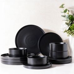 black plates and cups are sitting next to a vase with white flowers in the background