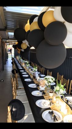 a long table is set with black and white plates, gold rimmed glasses, and balloons