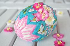 a decorative ball with flowers on it sitting on a wooden table next to pearls and beads