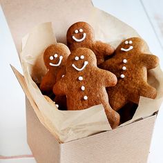 three ginger cookies in a box with white icing on them and some smiling faces