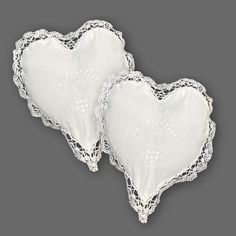 two white heart shaped pillows on a gray background, one is made out of lace and the other has an embroidered edge