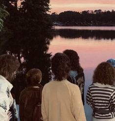 group of people standing near water watching the sunset