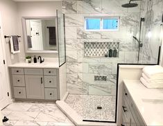 a white bathroom with marble counter tops and gray cabinets, along with a walk in shower