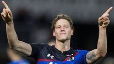 a male soccer player holding his hands up in the air with one hand and two fingers raised