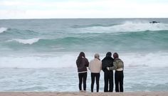 four people standing on the beach watching an airplane fly by