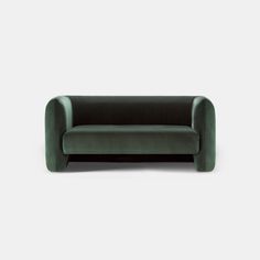 a green velvet couch sitting on top of a white floor next to a gray wall