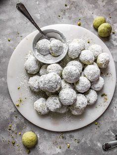 powdered sugar balls on a white plate with spoons and lemons around them