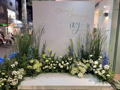 an arrangement of flowers and greenery on display in front of a grand opening sign