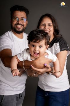 a man and woman holding a baby in front of a gray background with the caption's name on it