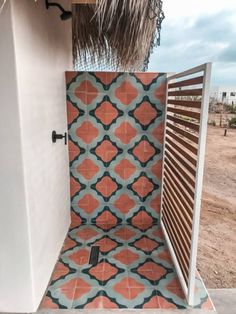 an outdoor shower with orange and blue tiles on the outside wall, next to a straw hut