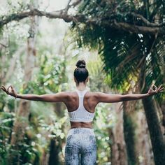 a woman is standing in the woods with her arms spread out and looking at the trees