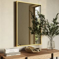 a mirror sitting on top of a wooden table next to a vase filled with plants