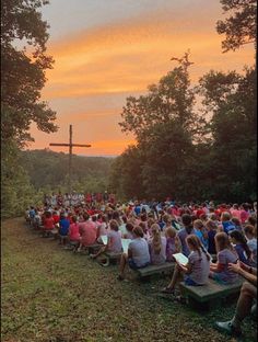 a large group of people sitting on benches in front of a cross at the top of a hill