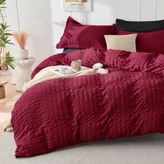 a bed with red comforter and pillows in a room next to a potted plant