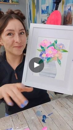 a woman holding up a painting with flowers in it