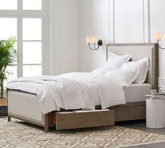 a bed with white linens and pillows in a room next to a potted plant