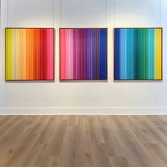 three colorful paintings hang on the wall in an empty room with wood floors and white walls