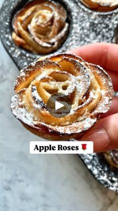 a hand holding an apple rose with powdered sugar on it in a muffin tin