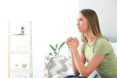 a woman sitting on the floor in front of a window with her hands clasped to her chest