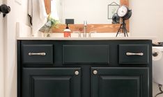 a bathroom vanity with black cabinets and a white toilet in front of a large mirror