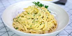 a white bowl filled with pasta and garnished with parsley on the side