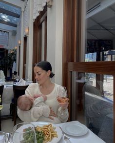 a woman holding a baby in her arms while sitting at a table with food and drinks