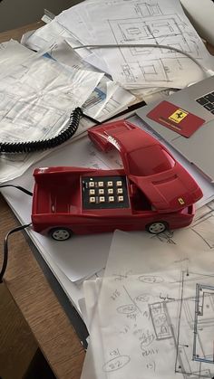 a red telephone sitting on top of a table next to papers and laptops with drawings