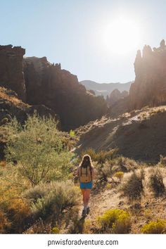 a woman hiking through the desert with mountains in the background and sun shining on her face