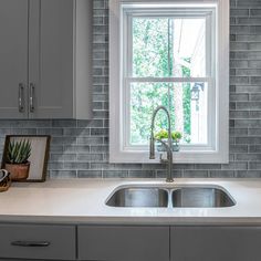 a kitchen sink sitting under a window next to a counter top with a potted plant