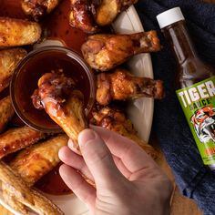 a person is dipping sauce on some chicken wings with a bottle of tiger juice in the background