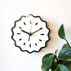 a black and white clock mounted to the side of a wall next to a potted plant