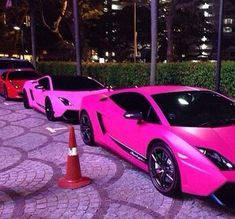 three pink sports cars parked next to each other on the side of a road at night