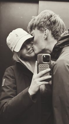 a man and woman kissing in front of a mirror while taking a selfie with their cell phone