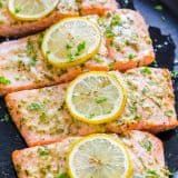 four pieces of salmon with lemons and parsley on them sitting on a black plate