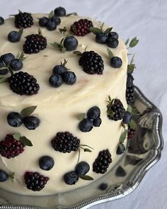 a cake with berries and blueberries on it is sitting on a silver platter